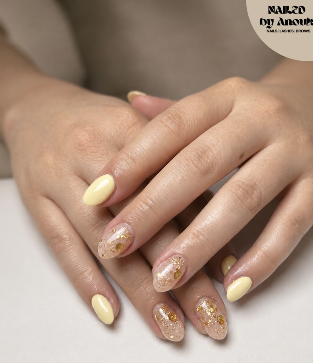 Handen over elkaar met pastelgele nagels en nagels met bladgoud