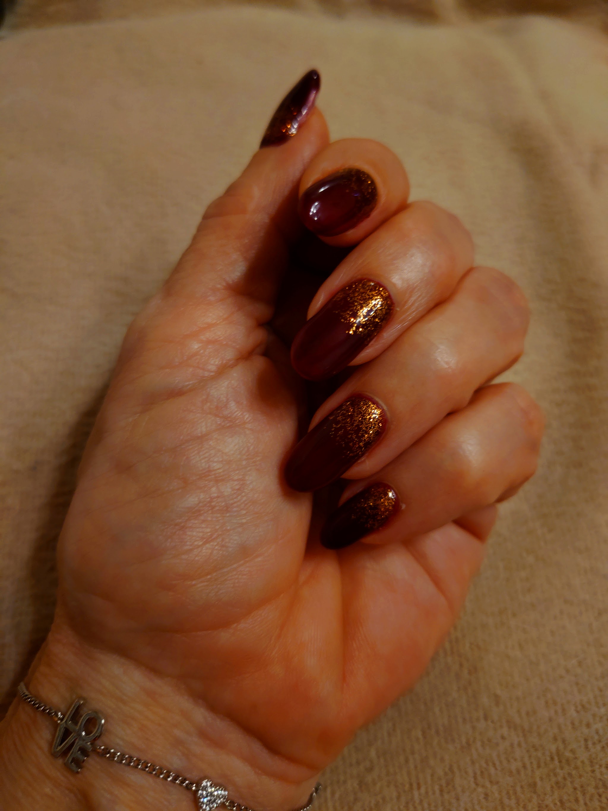 Hand met nagels in diep bruin en koperglitter